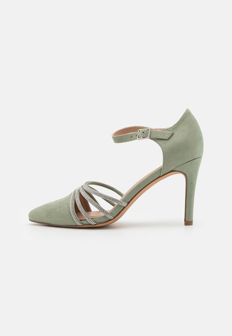 Chaussure à talon haut en daim vert avec un bout pointu, une bride à la cheville et des lanières décoratives en argent sur le devant. Texture lisse.