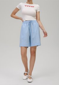 Světle modré kostkované šortky s elastickým pasem a šňůrkou, spárované s úzkým bílým tričkem s nápisem "VIVID" v červené barvě.