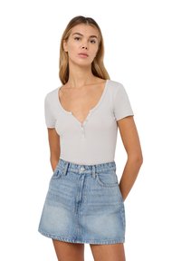 Maglietta henley a maniche corte, grigia chiara, con scollatura a V profonda e placket con tre bottoni, abbinata a una gonna di jeans alta vita in denim blu chiaro.