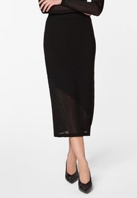 Jupe midi noire à côtes avec un panneau transparent diagonal, dotée d'une taille ajustée et d'une texture lisse. Associée à des escarpins noirs à bouts pointus.