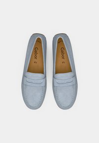 Γαλάζια σουέντ μοκασίνια με επίπεδη σόλα, με διακοσμητικό λουράκι και ραφές. Το εσωτερικό διαθέτει καφέ πέλμα με το όνομα της μάρκας.