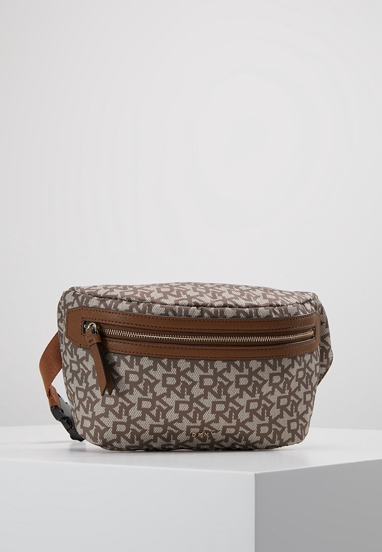 Sac banane en tissu marron monogrammé avec poche zippée à l’avant et sangle réglable, posé sur une surface blanche avec un fond neutre.