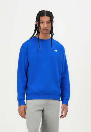 Blauwe sweatshirt gemaakt van zacht materiaal, met een ronde hals en ribbels aan de mouwen. Klein wit logo op het linker borstgebied.
