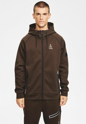 Brązowa bluza z kapturem na suwak wykonana z miękkiego materiału, z kapturem ze sznurkiem. Na piersi znajduje się logo, a przy zamkach błyskawicznych kontrastujące akcenty.