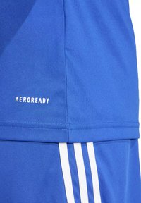 Gros plan sur un vêtement de sport bleu avec le texte blanc "AEROREADY" et trois bandes blanches verticales sur le tissu.