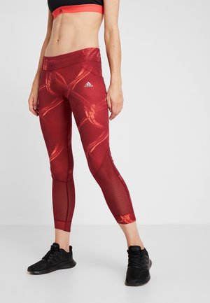 Leggings à motifs rouges et oranges avec des détails en mesh, taille haute et design ajusté. Logo Adidas sur le côté gauche. Matériau léger.