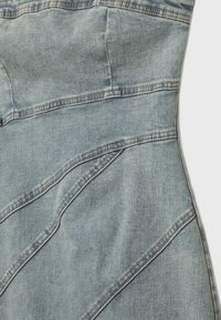 Denimmekko vaalean sinisenä, jossa on istuva vartalonosa, kulmatyyliset saumat ja erottuvat ompeleet. Pinta on sileä ilman näkyviä kuvioita.