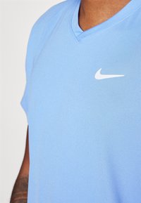 Ljusblå Nike v-ringad t-shirt med en mjuk textur och en liten vit swoosh-logotyp på vänster bröst. Korta ärmar, avslappnad design.