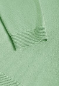 Gros plan d’un tissu tricoté vert clair montrant un poignet côtelé et une partie d’une manche.
