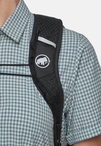 Zwarte rugzakband met gestructureerde padding, met een wit logo van een mammoet, bevestigd aan een blauw-wit geruit overhemd.
