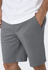 Grå træningsshorts med en blød tekstur, der har sidelommer og en komfortabel pasform. Kombineret med en enkel hvid T-shirt.