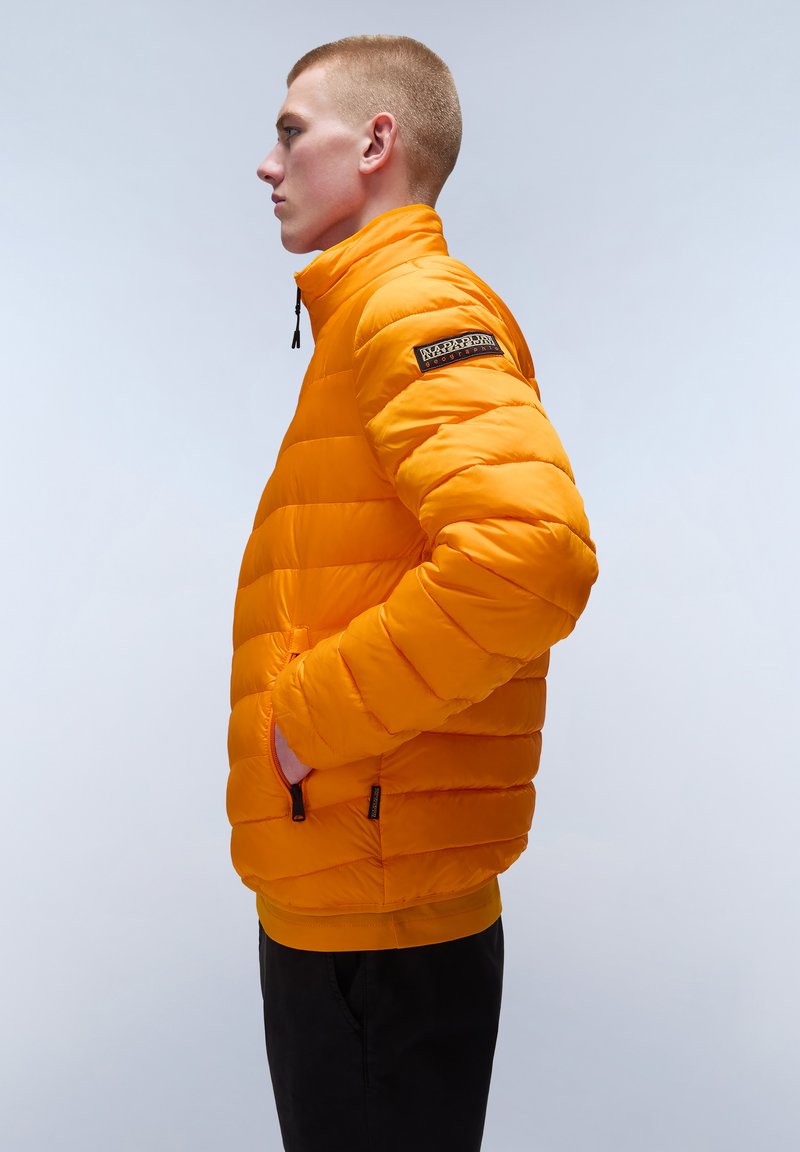 Kurtka puchowa w jasnym pomarańczowym kolorze, z poziomym wzorem pikowania, wysokim kołnierzem i kieszeniami bocznymi. Naszywka z logo na górnej części rękawa.
