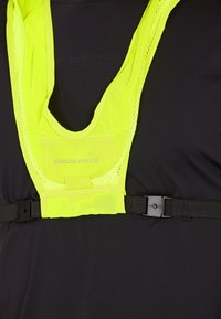 Fluoreszierende gelbe Netz-Sicherheitsweste mit verstellbaren schwarzen Trägern und einem auffälligen "ENDURANCE"-Logo auf der Vorderseite, getragen über einem schwarzen Shirt.