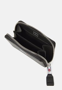 Cartera negra con cremallera hecha de cuero texturizado, que presenta dos compartimentos y una cremallera plateada. Etiqueta con el logo con acentos en azul, blanco y rojo.