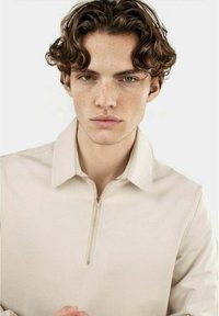 Pullover beige a zip a un quarto con una texture morbida, colletto e dettagli di cucitura minimi, caratterizzato da una leggera lucentezza e linee pulite.