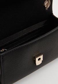 Black textured handbag interior with a zippered pocket and card slots. Features a gold metal clasp for secure closure.