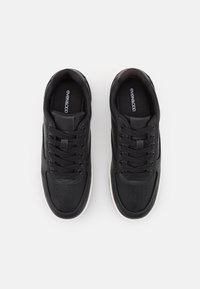 Zwarte sportschoenen met een gladleren bovenkant, ronde neus, geperforeerde details, platte veters en een witte rubberen zool. Merkl logo zichtbaar.