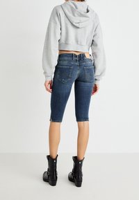 Sudadera corta gris con cuello ancho, combinada con pantalones cortos de mezclilla azul a la altura de las rodillas y botines negros con tacón grueso.