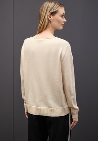 Cremfarbener, weicher Strickpullover mit lockerer Passform, geripptem Saum und Bündchen sowie weitem Halsausschnitt. Abgebildet auf einem Modell, von hinten betrachtet.