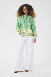 Blusa verde con motivo paisley, maniche lunghe, scollatura arricciata e dettagli intricati, abbinata a pantaloni bianchi a gamba larga e sandali marroni.