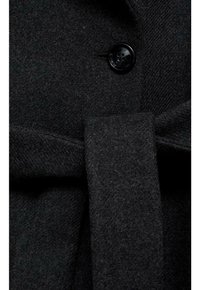 Manteau en laine noire avec un bouton et une ceinture en tissu nouée à la taille, montrant les détails de texture et de fermeture.