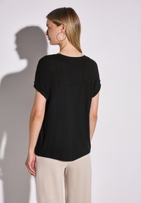 Sort top med korte ærmer, der har en struktureret strikket ryg og en glat front. Sæt sammen med lysebeige vidde bukser.