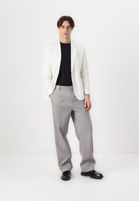 White blazer over a black T-shirt, paired with light gray pleated trousers and black shoes. Smooth fabric with a tailored fit.