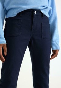 Mørkeblå bukser lavet af et blødt materiale, med to store forlommer, knaplukning og en slim-fit design.