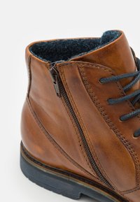 Bota de cuero marrón con forro de fieltro azul en contraste, que presenta una cremallera lateral, cordones grises y una suela texturizada.