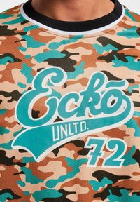 Majica s kratkim rukavima s bež, smeškim i teget kamuflažnim uzorkom, velikim belim logom "Eckó UNLTD." i brojem "72" u teget boji. Crna kragna.