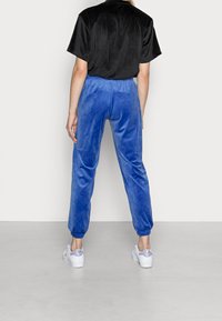 Svart kortärmad topp i kombination med blå sammetsoveraller. Overallerna har elastiska ärmslut och en texturerad yta, vilket kompletteras av vita sneakers.