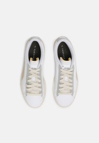 Vita sneakers med grå och beige detaljer, med en slät läderöverdel, rund tå, platt snörning och en texturerad gummisula.