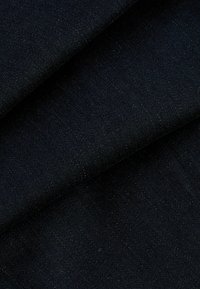 Dunkelblauer Denim-Stoff mit einer glatten Textur, der ein diagonales Webmuster und subtile Lichtreflexionen aufweist, in geschichteten Abschnitten gefaltet.