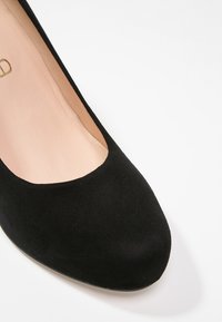 Ballerine femme en daim noir avec un bout arrondi et une doublure intérieure beige clair sur fond blanc.