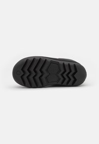 Suela de zapato de goma negra con un patrón de banda de rodadura en zigzag. Presenta un logotipo circular estampado y una superficie texturizada para mayor agarre.