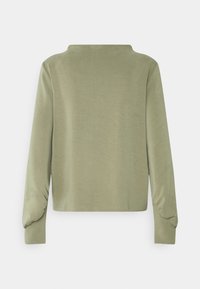 Haut vert clair à manches longues avec une coupe droite, un col légèrement relevé et un détail de tissu froncé près des poignets.