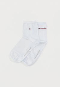 Λευκές βαμβακερές κάλτσες αστραγάλου με ένα μικρό λογότυπο σε κόκκινο, λευκό και μπλε, με εναλλασσόμενη ριγέ ταινία και τυπωμένο όνομα μάρκας στην πλευρά.