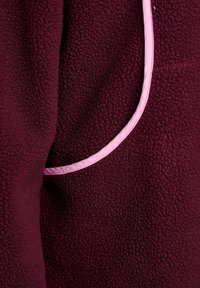 Burgundia fliiskangas, millel on tekstureeritud pind, kerge roosa äärisega servade ümber ja küljetasku.