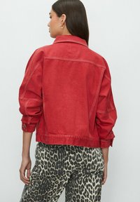 Red denim jacket with a relaxed fit, featuring a pointed collar and detailed stitching. Paired with black and white animal print pants.
