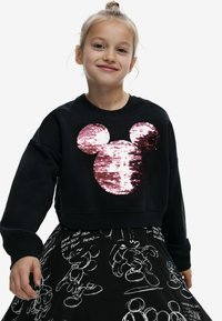Schwarzer verkürzter Sweatshirt mit einer großen pinkfarbenen Pailletten-Silhouette von Mickey Mouse. Kombiniert mit einem schwarzen Rock, der weiße Cartoon-Skizzen zeigt.