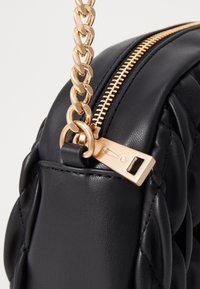 Borsa a tracolla in pelle nera con texture trapuntata, tracolla in catena dorata e dettagli con zip dorata. Accentuata da un tirazip rettangolare.