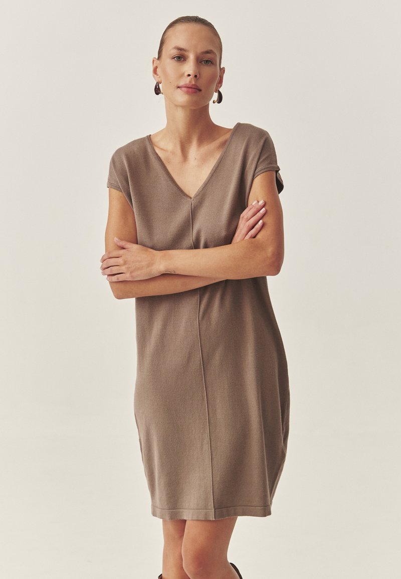 Braunes Kurzarmkleid aus weichem Strickstoff mit einem V-Ausschnitt, das über eine Nahtdetail in der Vorderseite und einen lockeren Schnitt verfügt, der bis zur Mitte des Oberschenkels reicht.