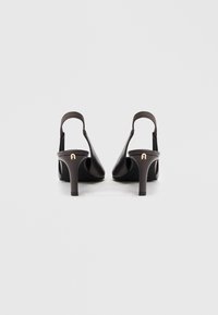 Μαύρα ψηλοτάκουνα παπούτσια slingback από δέρμα με υφασμένη πίσω λουρίδα και λεπτό, μεσαίου ύψους τακούνι. Διαθέτουν χρυσή διακοσμητική λεπτομέρεια με λογότυπο στο τακούνι.