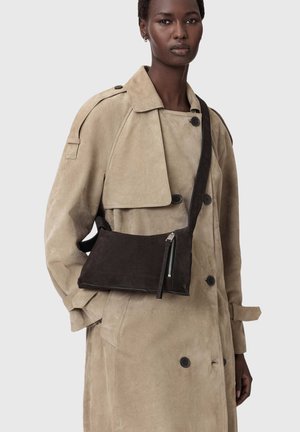 Femme portant un trench-coat en daim beige avec un sac bandoulière en daim noir orné d'une fermeture éclair.