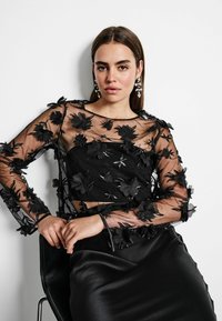Zwart mesh top met lange mouwen versierd met textuur florale appliqués, gecombineerd met een gladde zwarte satijnen rok die een aansluitende silhouet toont.