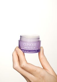 Baume nettoyant CLINIQUE dans un pot transparent violet, avec du texte blanc. Le pot est tenu dans une main, dévoilant un design de conteneur lisse et rond.