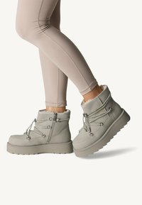 Bottines grises avec doublure en fausse fourrure, bout rond et semelle en caoutchouc épaisse. Caractérisées par un matériau texturé et des lacets métalliques avec des zips sur les côtés.