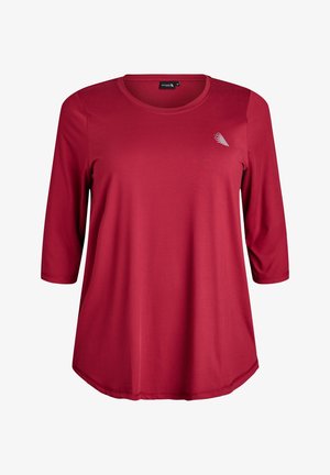 Sarkans garām piedurknēm, ar apaļu kakla izgriezumu un izliekta apakšmala, izgatavots no gludas auduma. Uz krūšu daļas ir neliels balts grafisks elements.