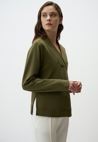 Maglia a maniche lunghe verde oliva con scollatura a V, fessure laterali e vestibilità comoda, realizzata in un tessuto morbido e liscio.