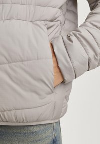 Light gray puffer jacket with quilted texture, side pockets, and elastic cuffs. Material appears smooth and slightly shiny.